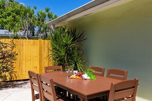 An outdoor patio with a wooden table and chairs, surrounded by a wooden fence and greenery. - Buttonwood Corner | Midtown Key West • Pool + Tropical Patio | Near Beaches (Key West)
