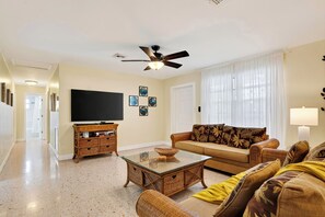 A living room with a television, sofa, and a ceiling fan. - Buttonwood Corner | Midtown Key West • Pool + Tropical Patio | Near Beaches (Key West)