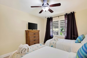 A hotel room with two beds, a ceiling fan, a television on a dresser, and a window with curtains. - Buttonwood Corner | Midtown Key West • Pool + Tropical Patio | Near Beaches (Key West)