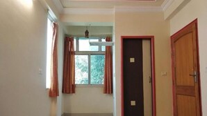 Una habitación con cama, ventana con cortinas, puerta y lámpara en el techo.