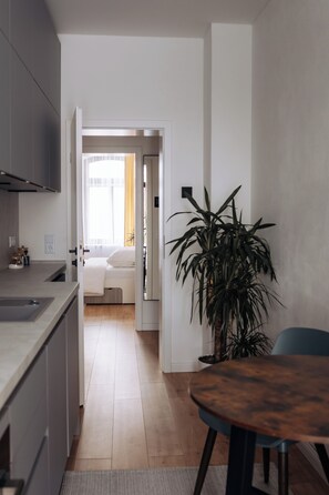 Eine moderne Küche mit Essbereich, einer großen Topfpflanze und Blick in ein Schlafzimmer durch eine offene Tür.