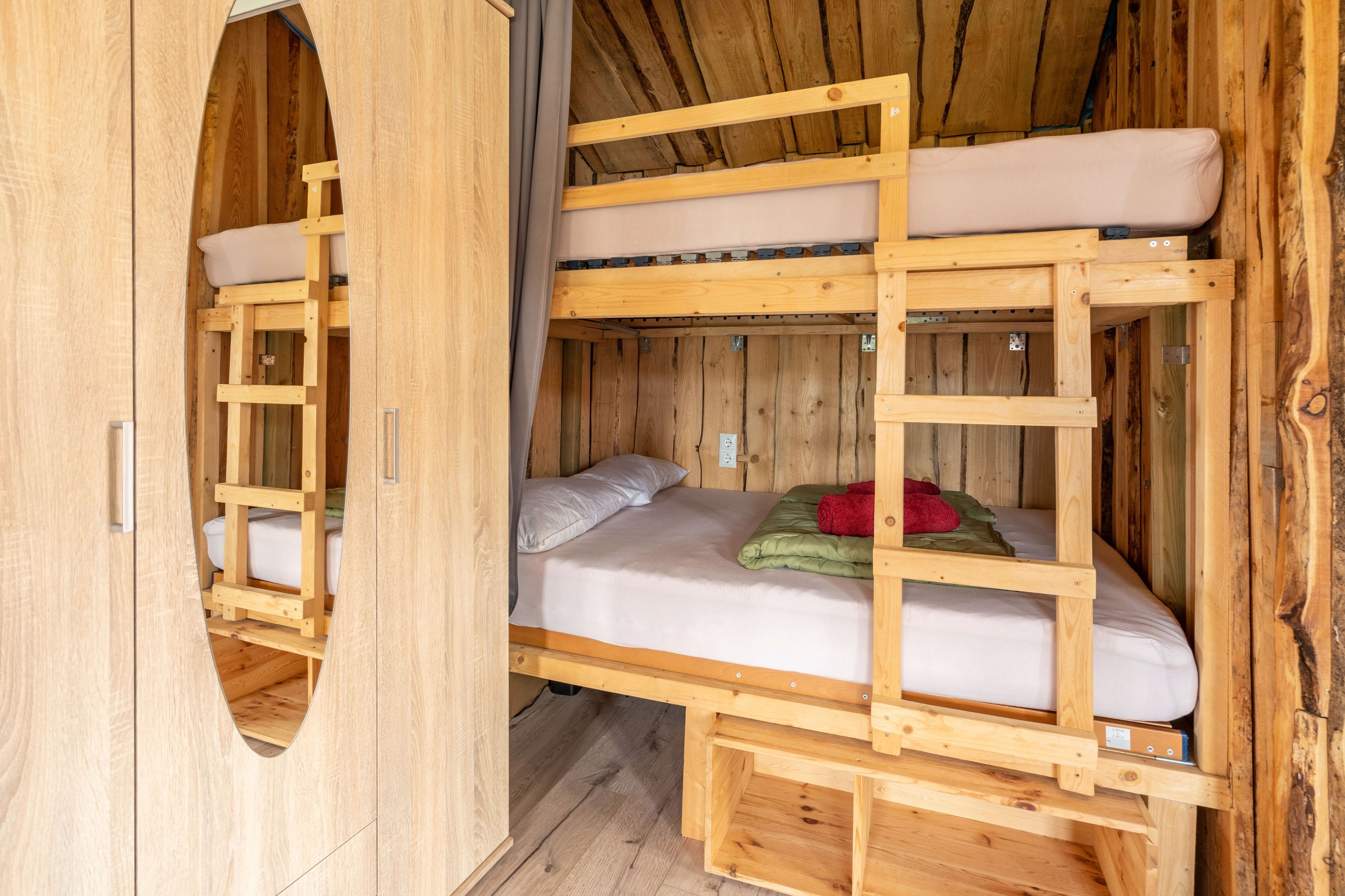 Ein Zimmer mit einem hölzernen Etagenbett, einer Leiter, einer Matratze und einer Decke.