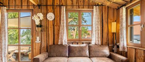 A wooden interior with a sofa, a table with a decorative item, and a clock on the wall.