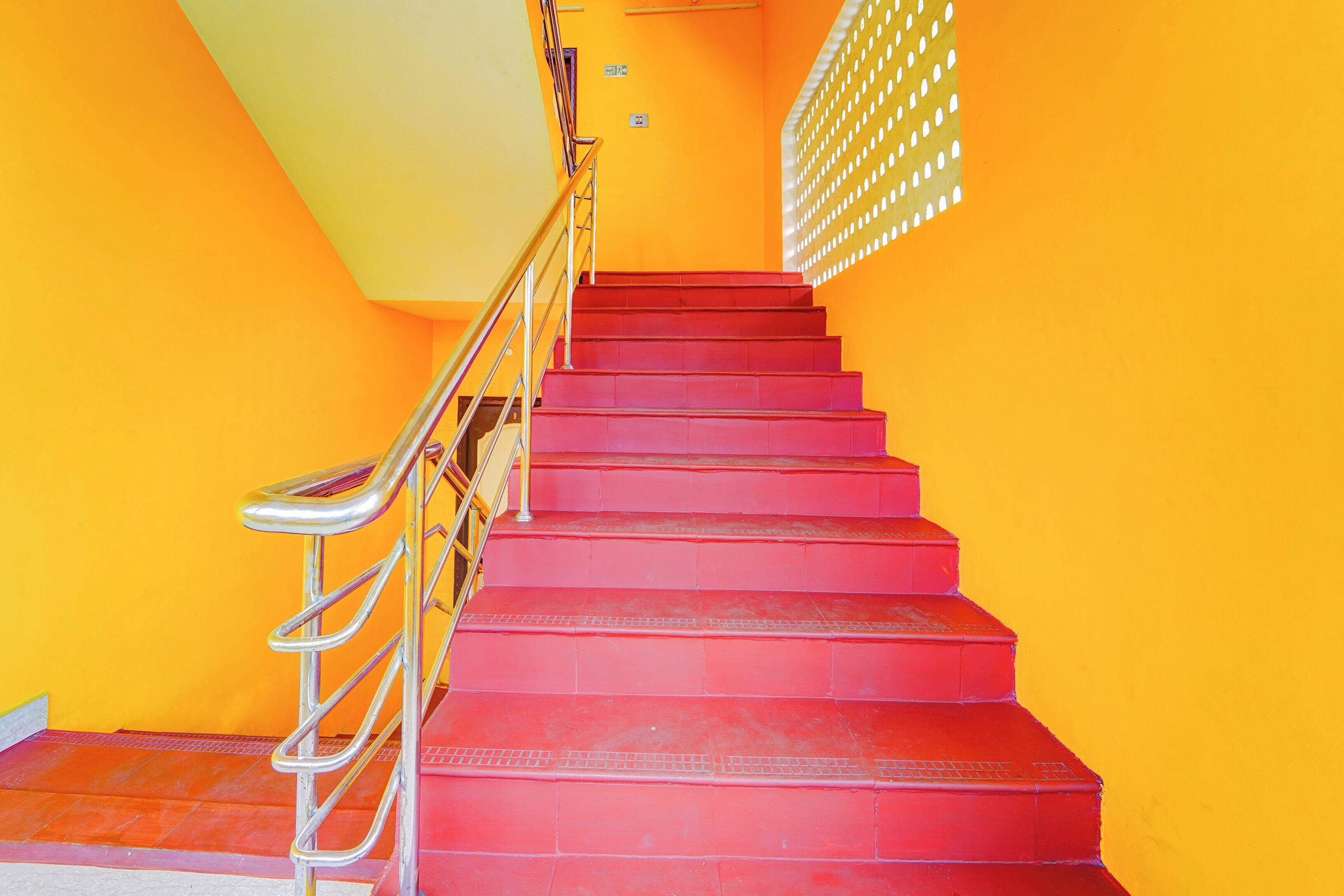 A staircase with red steps and a metal railing, leading to a door with a yellow wall and a window with a grid pattern.