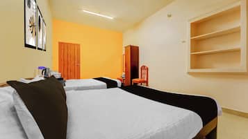 Quarto de hotel com duas camas, uma porta de madeira, uma mesinha com chaleira e uma estante.