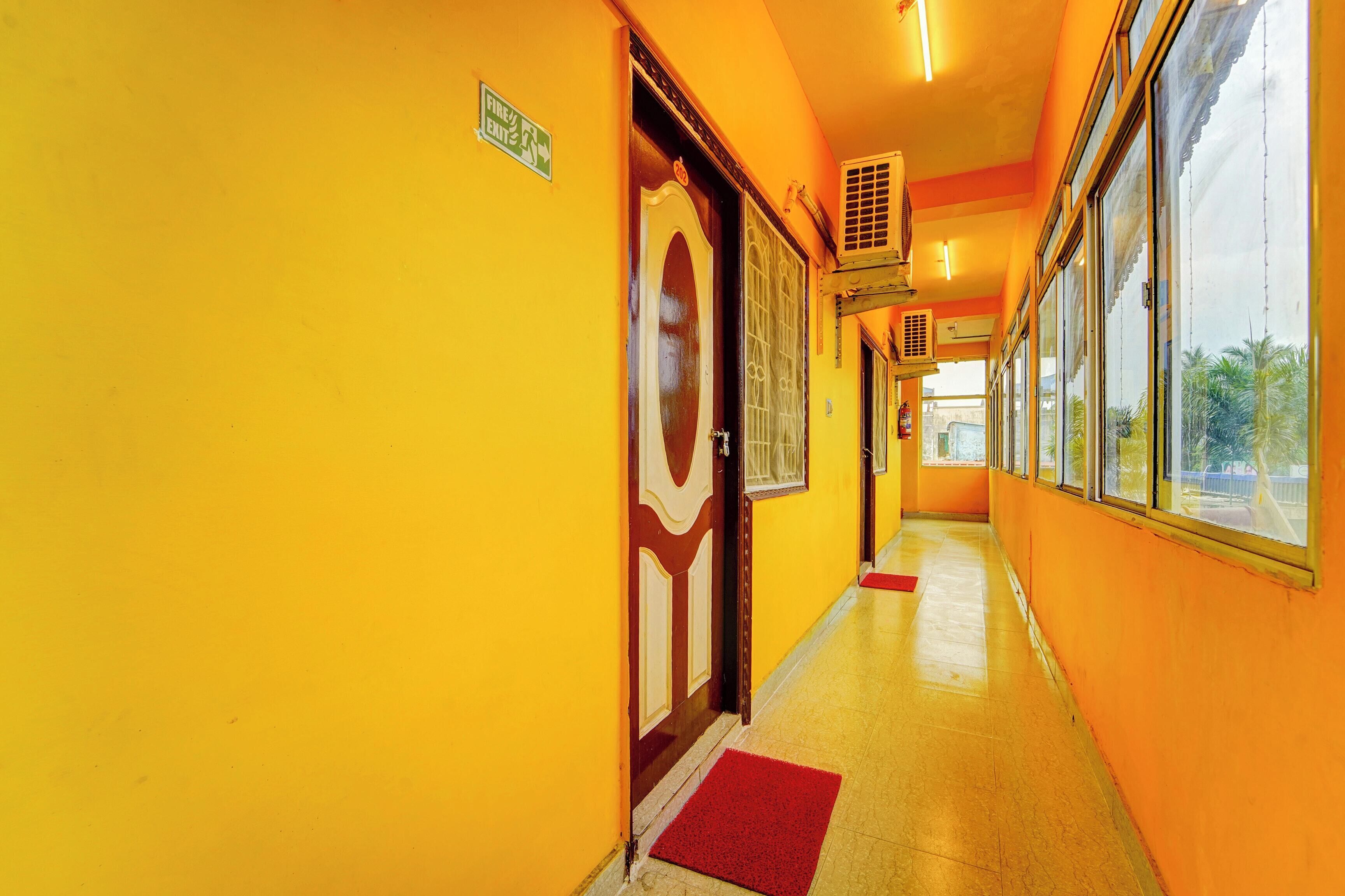 A corridor with yellow walls, a fire exit sign, and a door with a decorative glass panel.