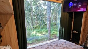 Un dormitorio con un ventanal grande, una cama, un televisor y techo de madera.