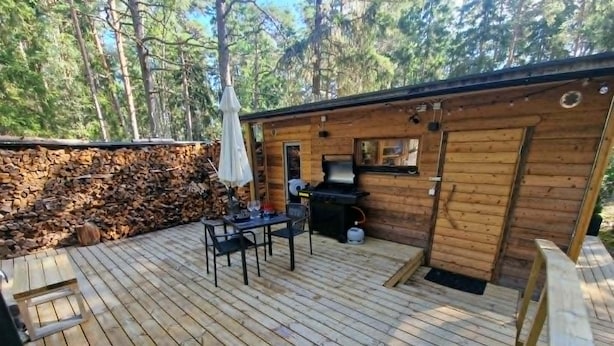 Una terraza de madera con una mesa, sillas, una parrilla y un muro de piedra.