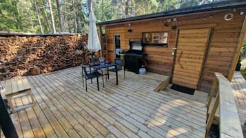 A wooden deck with a table and chairs, a barbecue grill, and a stone wall.