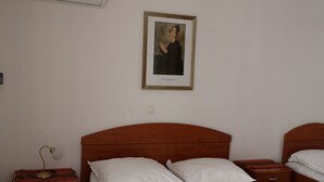 Una habitación de hotel con una cama, dos mesitas de noche, un aire acondicionado y un cuadro en la pared.