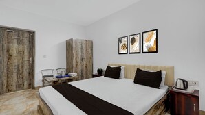 Habitación de hotel con cama, armario, escritorio con silla y mesita de noche con tetera y tazas.