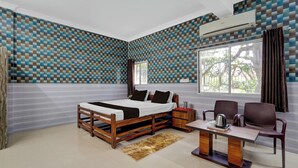 Un dormitorio con una cama, una mesita con hervidor, dos sillas y una ventana con cortinas.