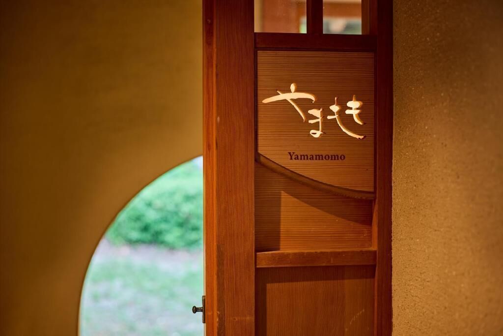Una puerta de madera con una placa que dice 'Yamamoto' y una vista parcial de un ventanal circular.