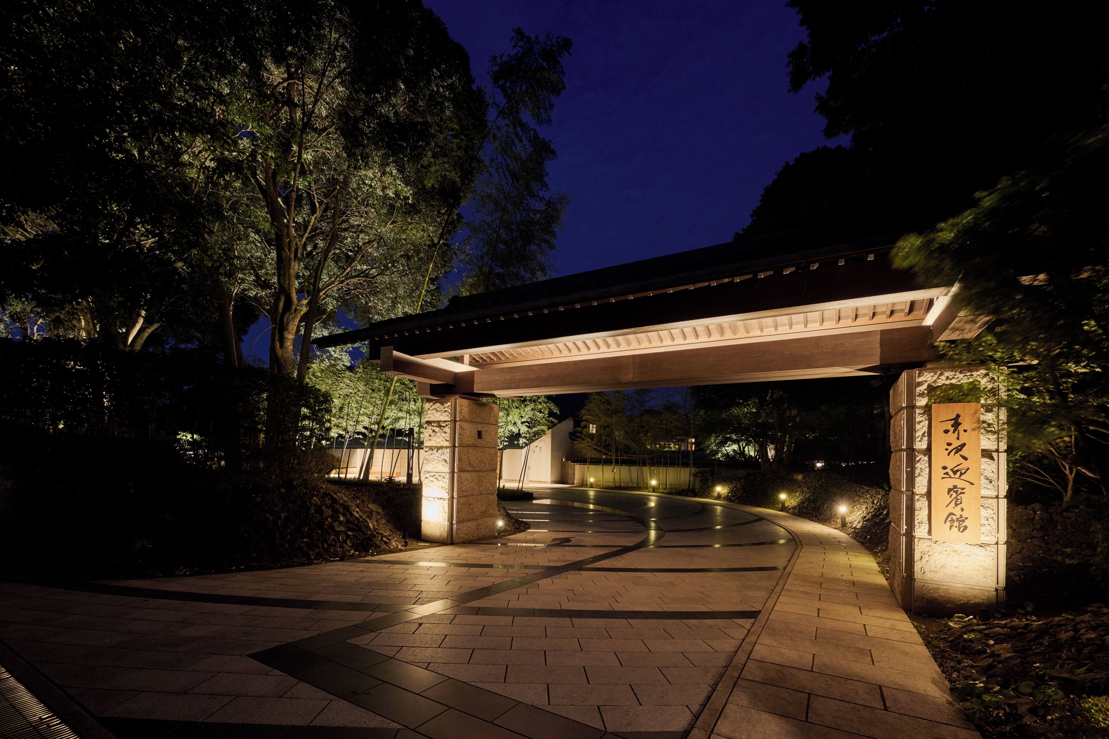 A covered walkway with stone pillars and a tiled floor, surrounded by trees.