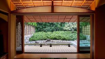 Um quarto japonês tradicional com tatames, uma porta deslizante para um jardim e teto de madeira.