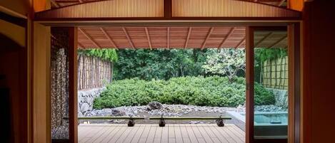 A traditional Japanese room with tatami flooring, a sliding door leading to a garden, and a wooden ceiling.