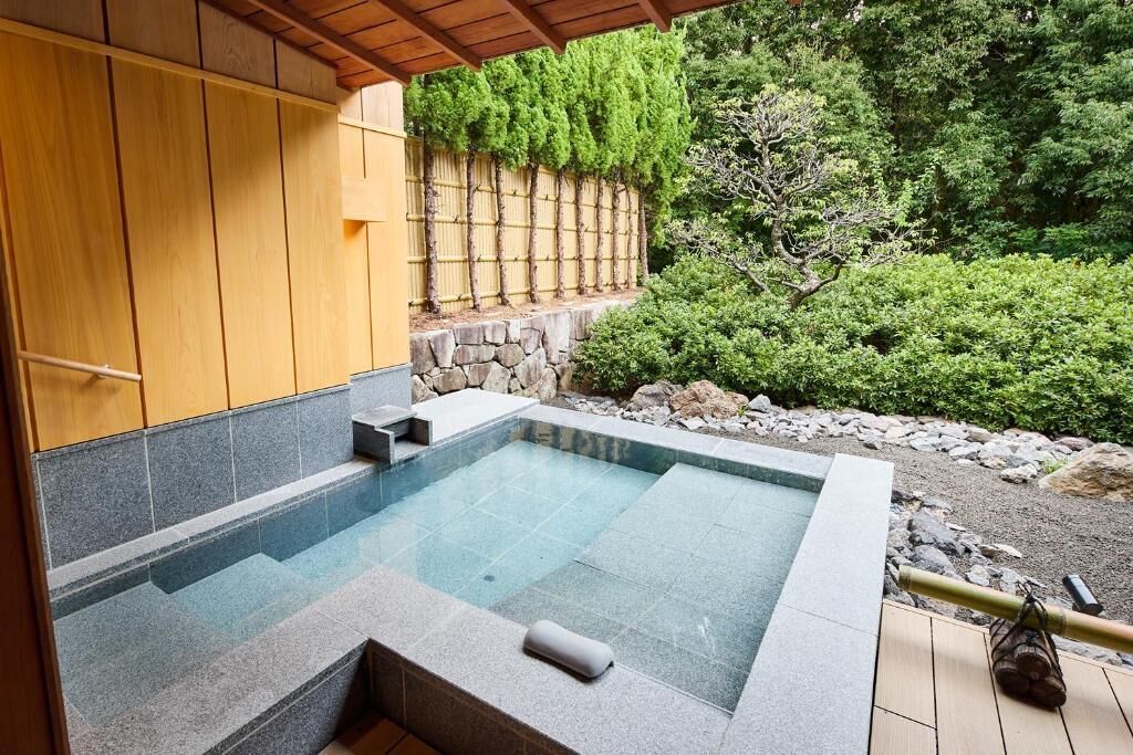 A hot tub with a stone surround, wooden deck, and a bamboo rake.