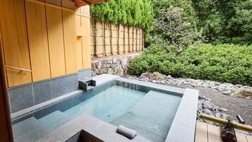 A hot tub with a stone surround, wooden deck, and a bamboo rake.