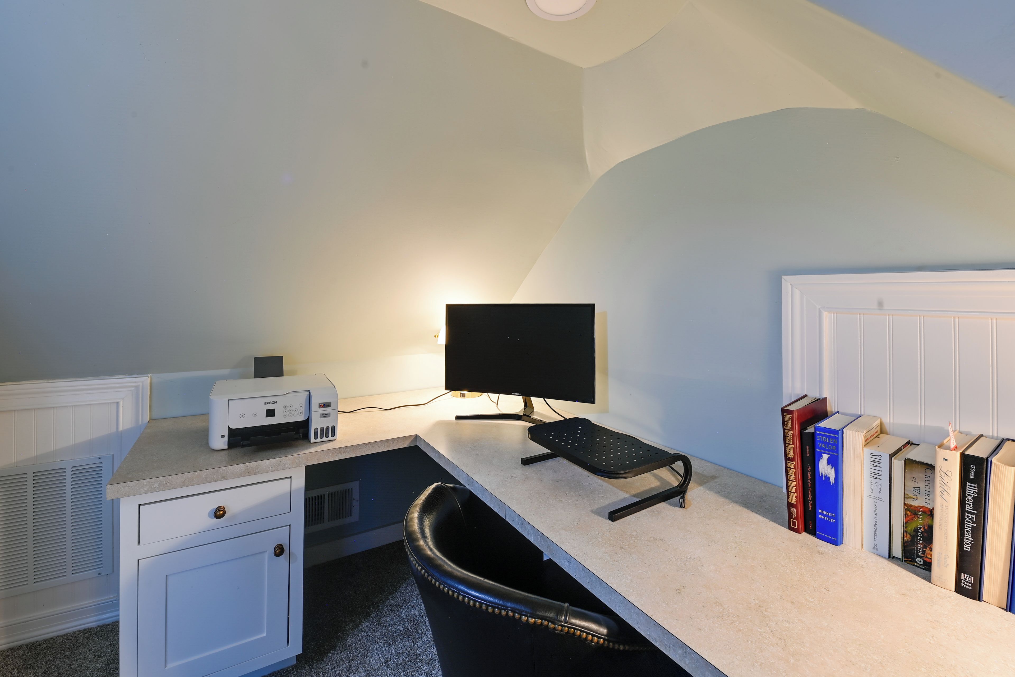 Een werkplek aan huis met een bureau, computer, stoel en boekenplanken.