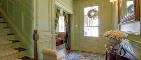Una gran escalera que conduce a una puerta con un arreglo floral sobre una consola.