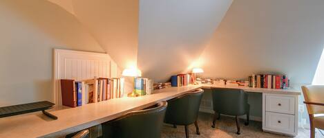 Una sala de estudio con escritorio, sillas, libros y dos lámparas.