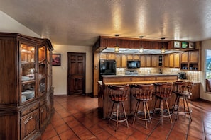 A kitchen with wooden cabinets, a central island with bar stools, a refrigerator, and a microwave. - Hike & Ski! Quiet Home w/ Solarium in Cloudcroft (Cloudcroft)