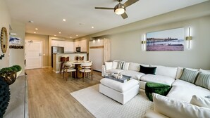 A modern living room with a white sofa, a coffee table, and a dining area with a round table and chairs. - Steps to the Sand! Luxury Oceanside Pier Condo (Oceanside)