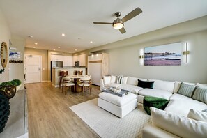 A modern living room with a white sofa, a coffee table, and a dining area with a round table and chairs. - Steps to the Sand! Luxury Oceanside Pier Condo (Oceanside)