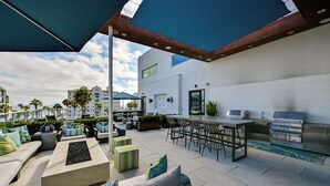 An outdoor patio with a bar and grill area, seating arrangements, and a view of the surrounding buildings. - Steps to the Sand! Luxury Oceanside Pier Condo (Oceanside)