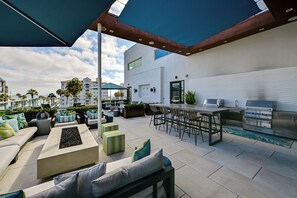 An outdoor patio with a bar and grill area, seating arrangements, and a view of the surrounding buildings. - Steps to the Sand! Luxury Oceanside Pier Condo (Oceanside)