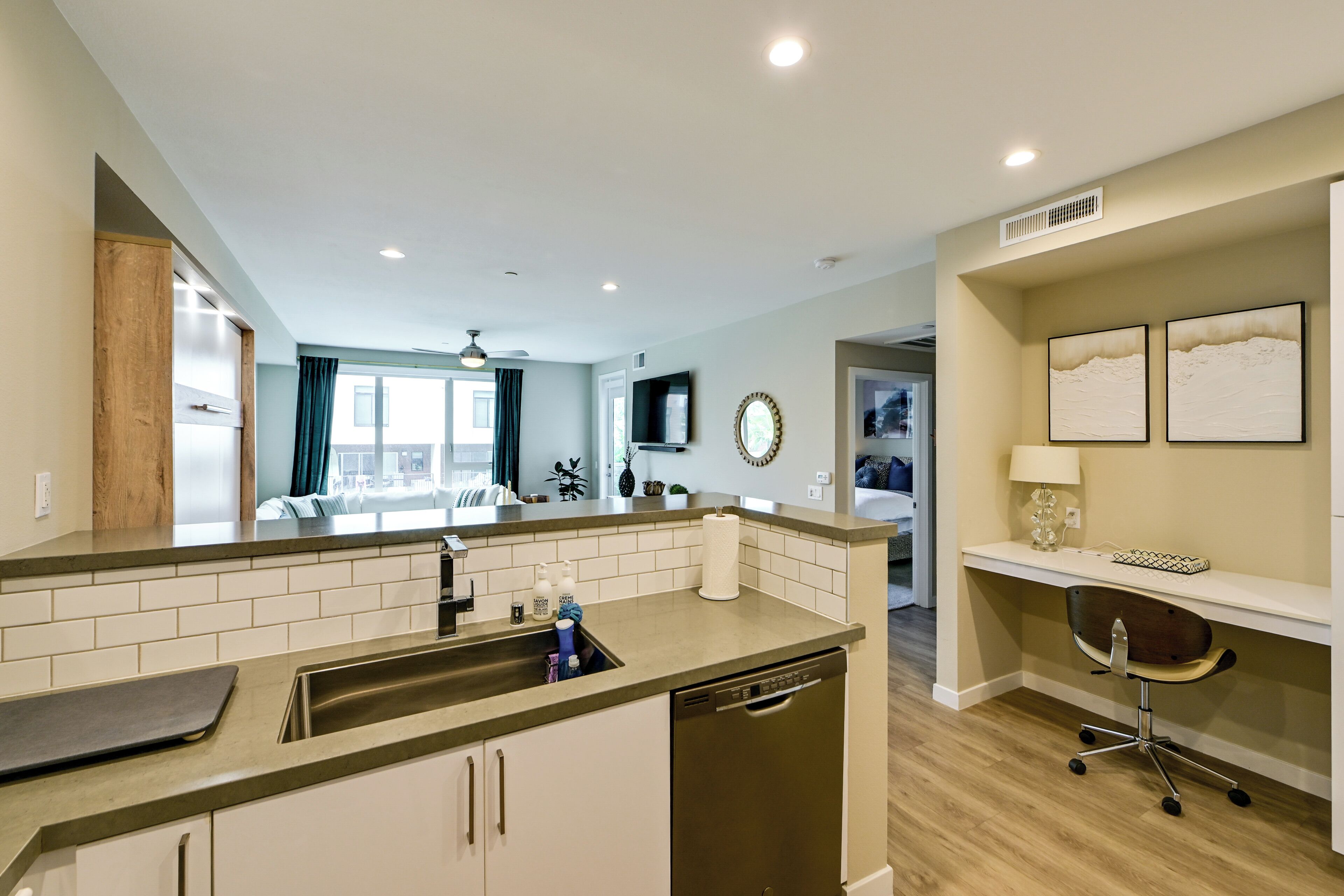 A modern kitchen with a dishwasher, a sink, and a countertop. There is a dining area with a table and chairs visible in the background.