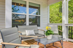 Eine überdachte Veranda mit einer Sitzecke, bestehend aus einer Couch, Sesseln, einem Glastisch und einem Blumentopf.