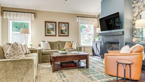 A living room with a sofa, armchair, coffee table, fireplace, and a television mounted above it. - Walk to Dtwn Waynesville! Dual Mtn Havens w/ Decks (Waynesville)
