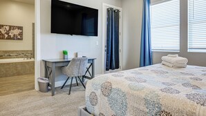 Ein Schlafzimmer mit einem Bett, einem Schreibtisch, einem Fernseher, einem Badezimmer mit einer Badewanne und einem Fenster mit Vorhängen.