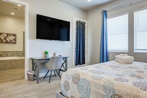 A bedroom with a bed, a desk, a television, a bathroom with a bathtub, and a window with curtains. - Private Swim Spa & EV Charger! By Tuacahn and more (Santa Clara)
