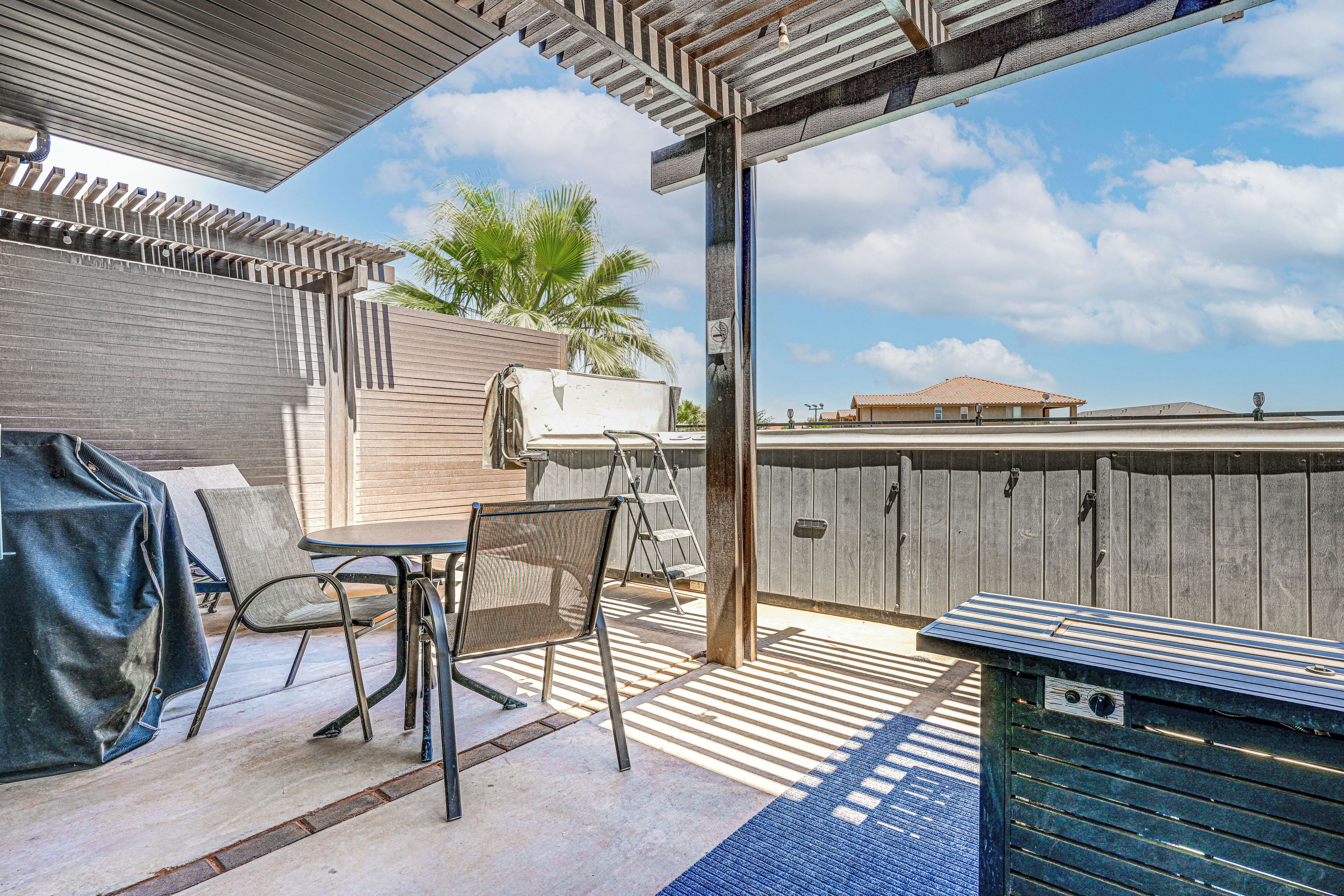 A covered patio area with a table and chairs, a grill, and a wooden fence.