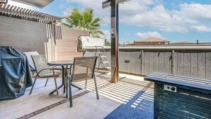 Ein überdachter Patio-Bereich mit Tisch, Stühlen, einem Grill und einem Holzzaun.