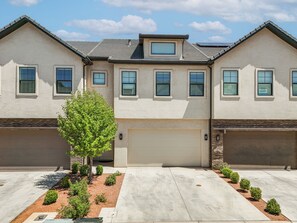 A two-story house with a garage, a small tree in the driveway, and a clear sky. - Private Swim Spa & EV Charger! By Tuacahn and more (Santa Clara)
