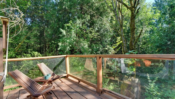 Une terrasse en bois avec une rambarde en verre donnant sur une zone boisée.
