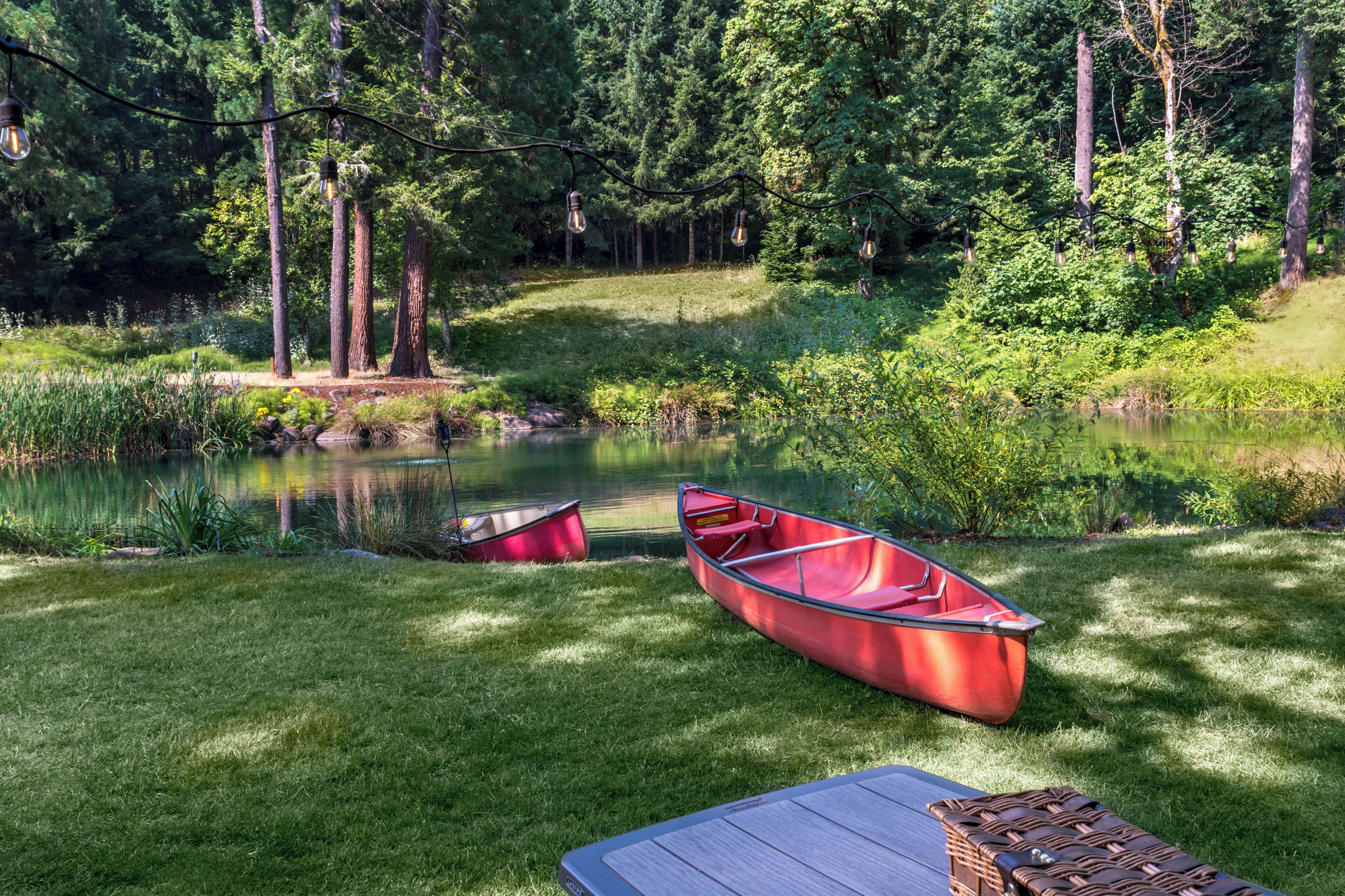 A serene lakeside setting with a red boat and a picnic table on the grass.