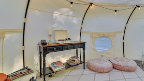 A tent interior with a table, books, a candle, and two ottomans.