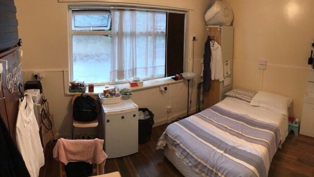 Een slaapkamer met een bed, bureau, stoel, raam en een kledingkast.