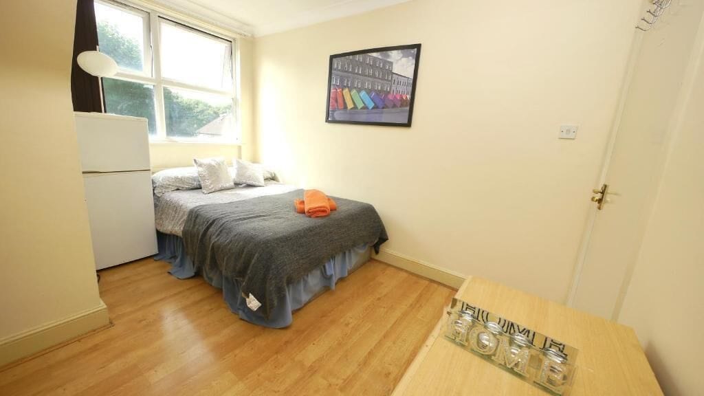 A bedroom with a bed, a small table, a window, and a door.