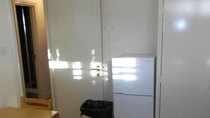 Een kleine keuken met een koelkast, een prullenbak en een houten tafel met stoelen.