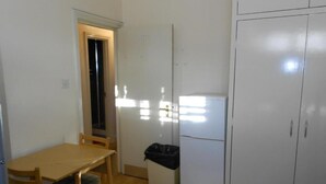 Een compacte keuken met een koelkast, een prullenbak en een houten eettafel met stoelen.