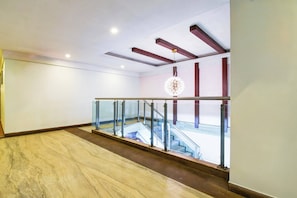 Un interior espacioso con piso de mármol, baranda de vidrio y una escalera que conduce a un espacio exterior.