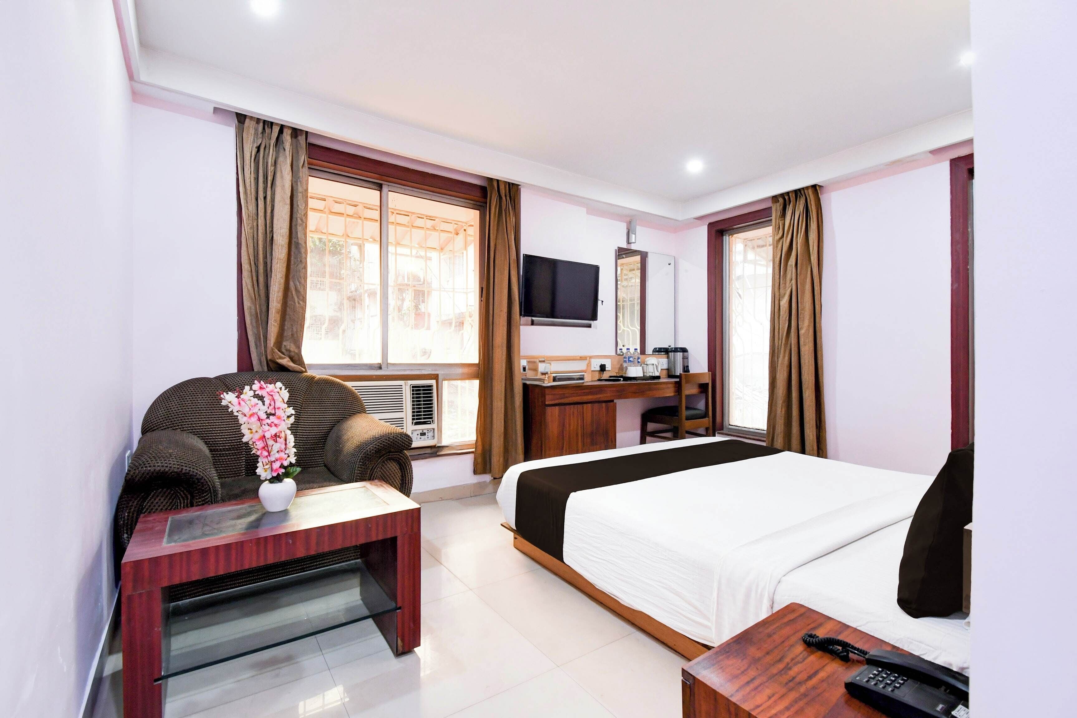 Quarto de hotel com cama, escrivaninha, televisão e janela com cortinas.