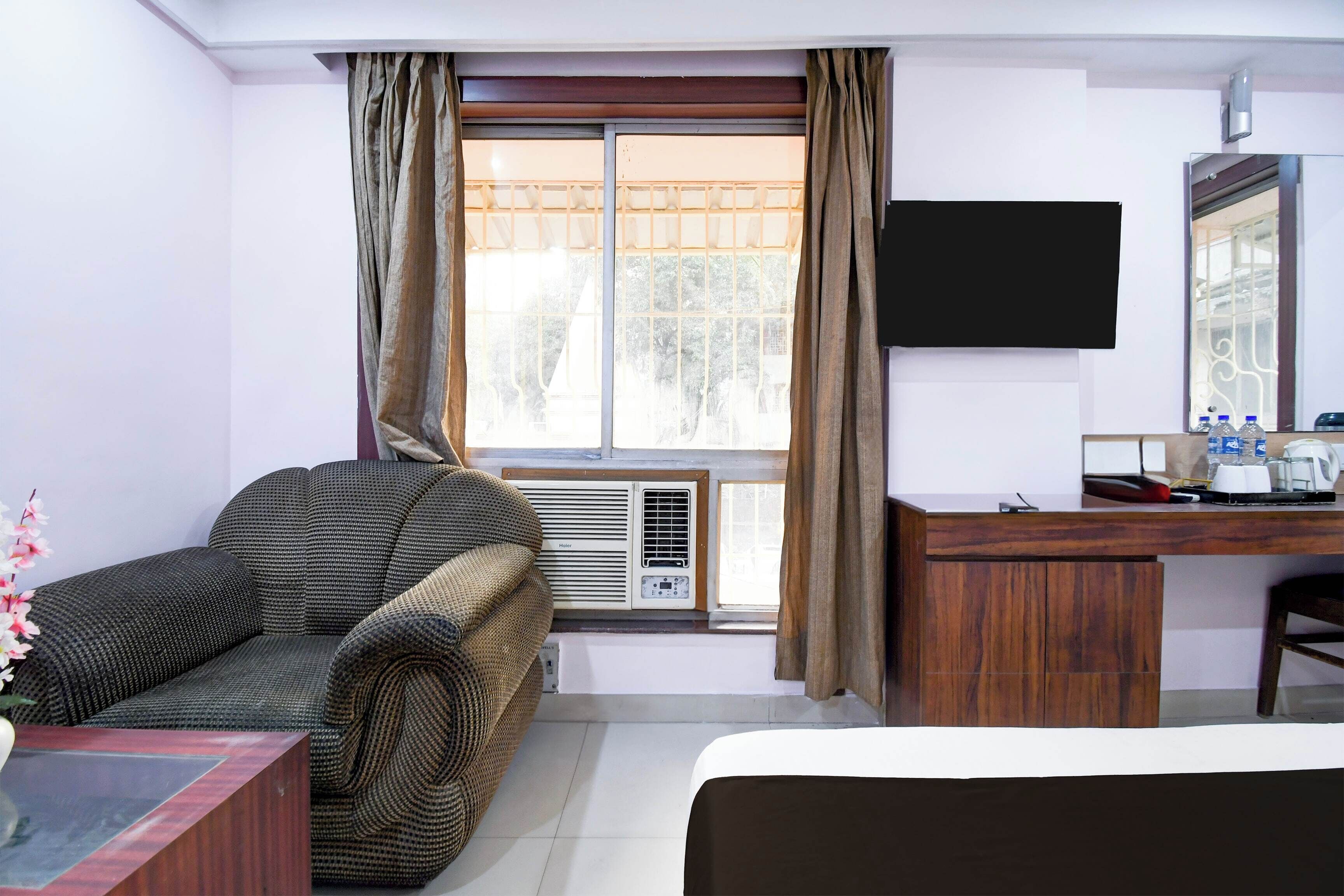 Quarto de hotel com sofá, secretária, televisão de tela plana, cama e janela com cortinas.