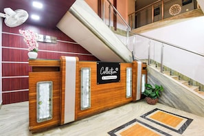 Mostrador de recepción con un cartel que indica servicio de recolección, una escalera y un área de recepción con un arreglo floral.