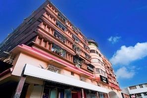 Un edificio de varios pisos con balcones, un cartel que indica servicio de recolección y un cielo azul despejado.